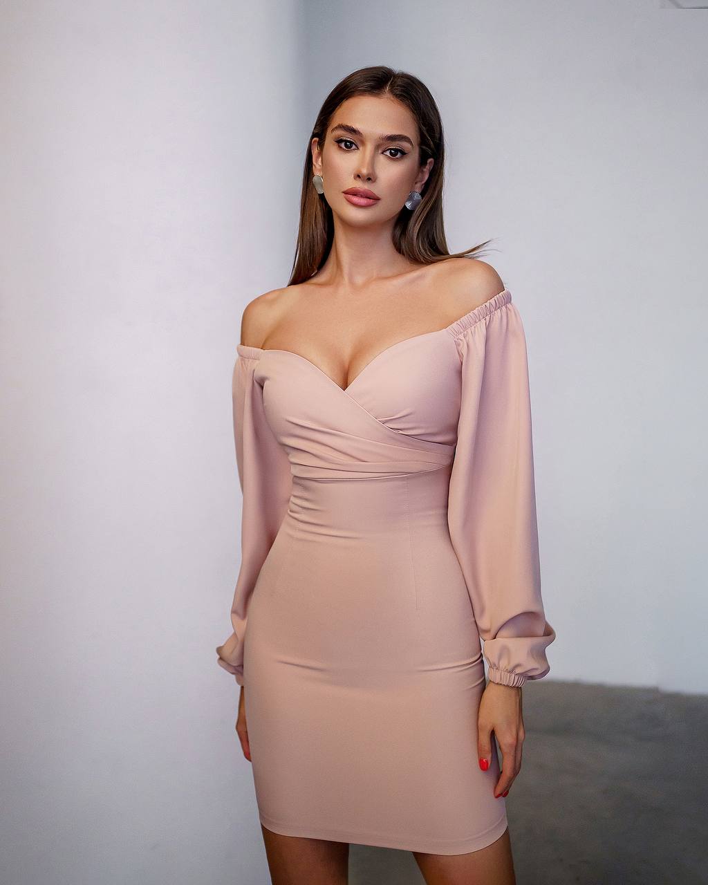 Woman wearing a pink off-shoulder dress against a plain background