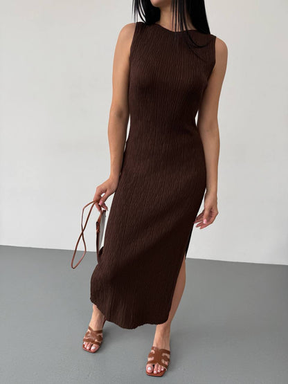 Woman wearing a brown sleeveless dress holding a matching handbag against a plain background