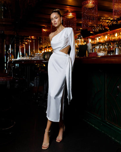 Woman in a white dress standing in a dimly lit bar.