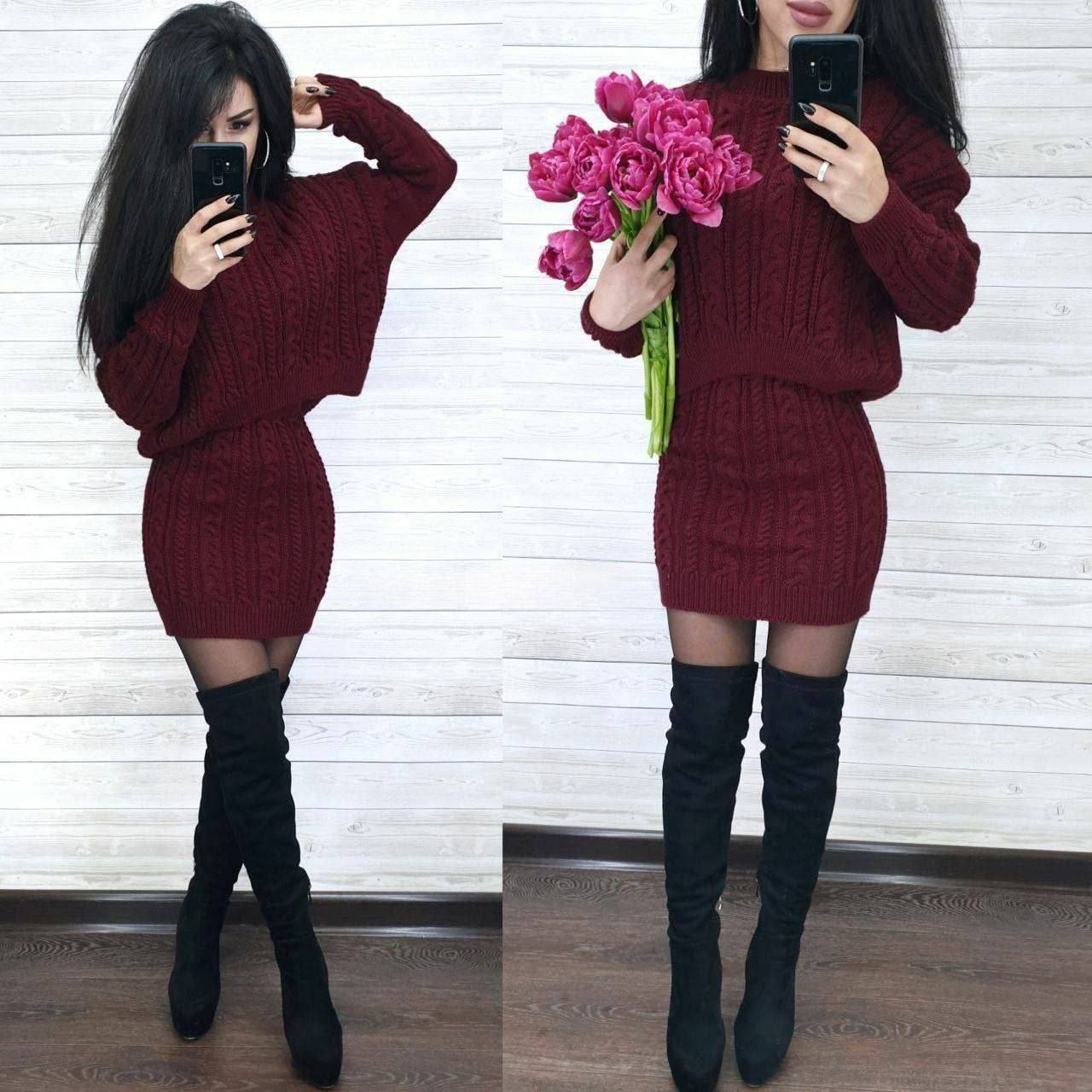 Woman wearing a burgundy cable knit dress with black knee-high boots, holding pink flowers.