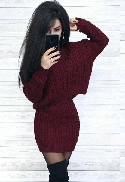 Person wearing a burgundy cable knit sweater dress against a white wooden panel background