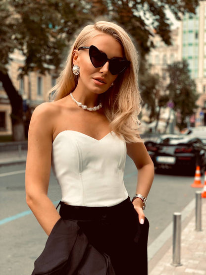 Woman in a white top and black pants standing on a city street.