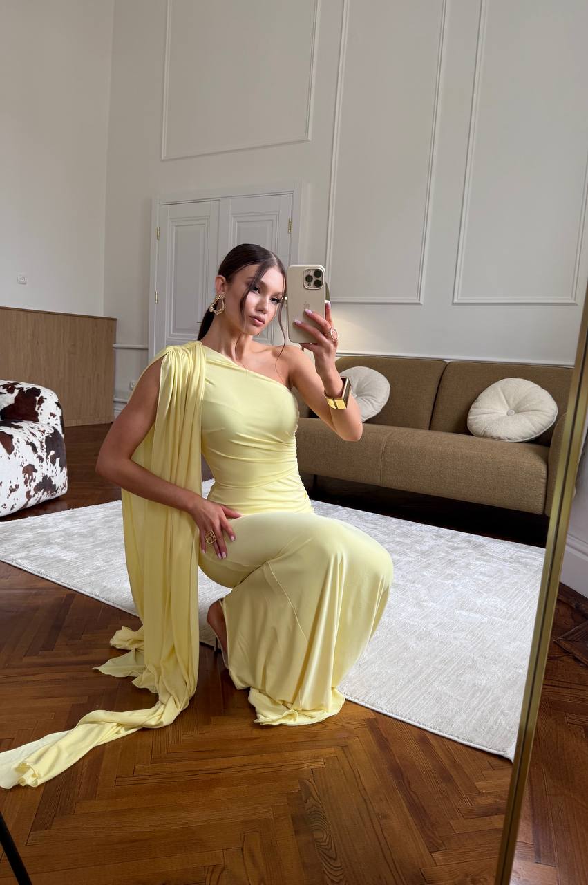 Woman in a yellow dress taking a mirror selfie in a room with a couch and rug.