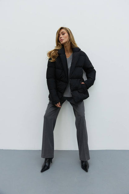 Woman wearing a black puffer jacket and gray pants against a white background
