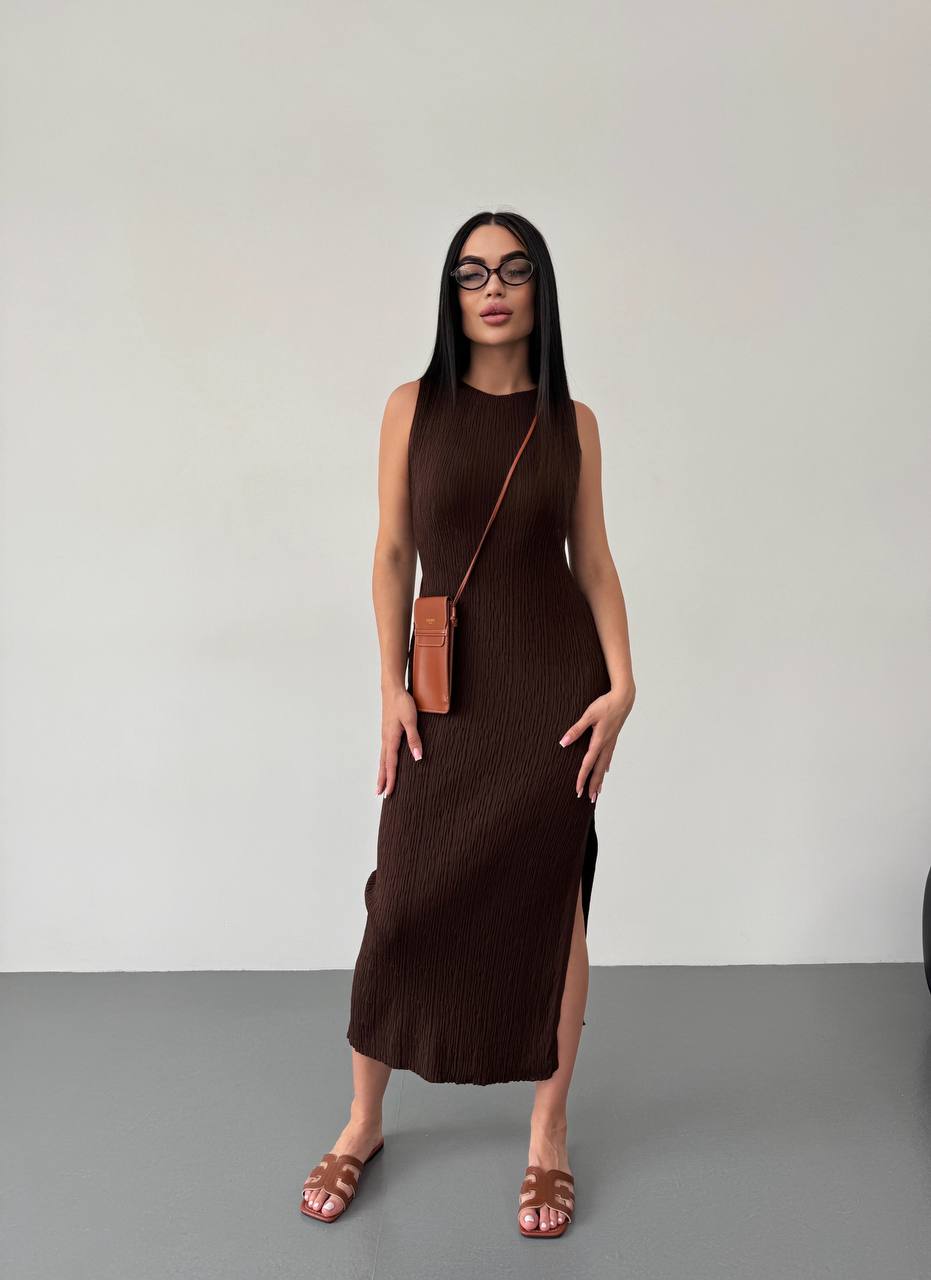 Woman wearing a brown sleeveless dress with a matching handbag against a plain background