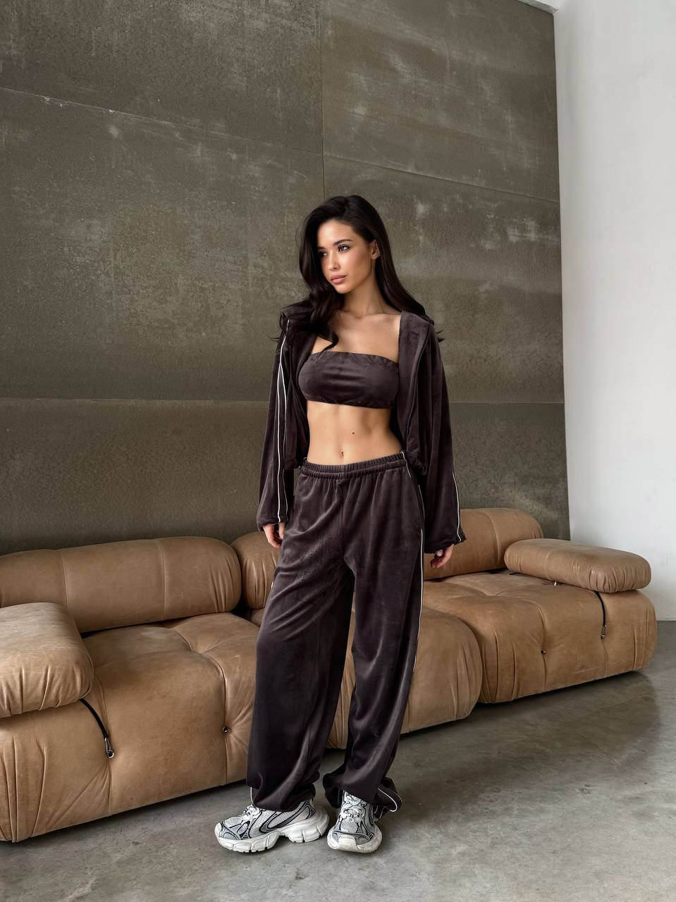 Woman in dark outfit standing in a modern living room with a brown sofa.