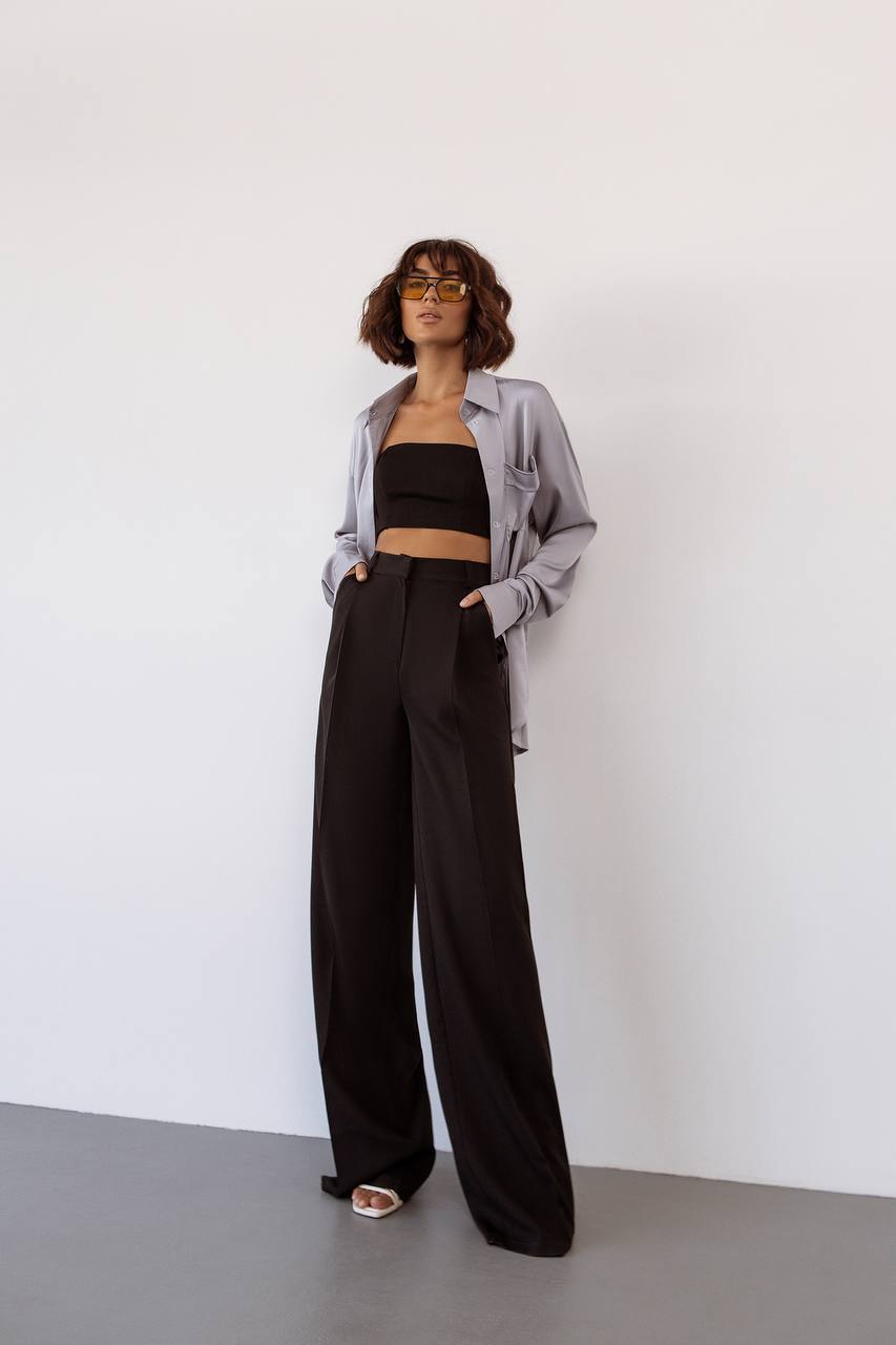 Woman wearing a black top and wide-leg pants with a light gray shirt against a white background