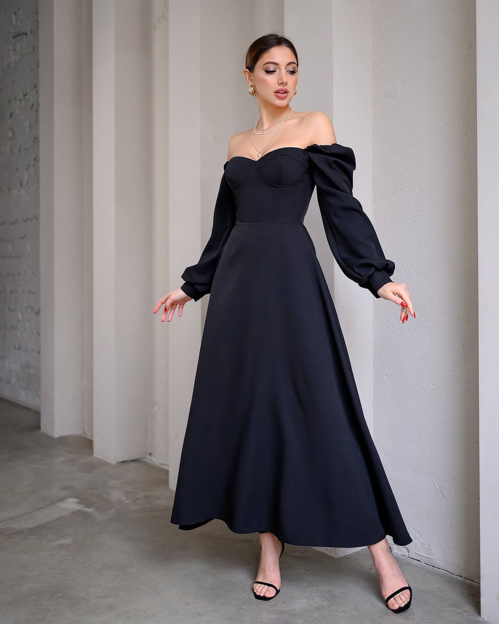 Woman wearing a black off-shoulder gown with puffed sleeves against a neutral background