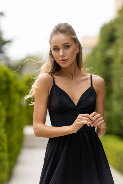 Woman wearing a black dress standing outdoors with greenery in the background