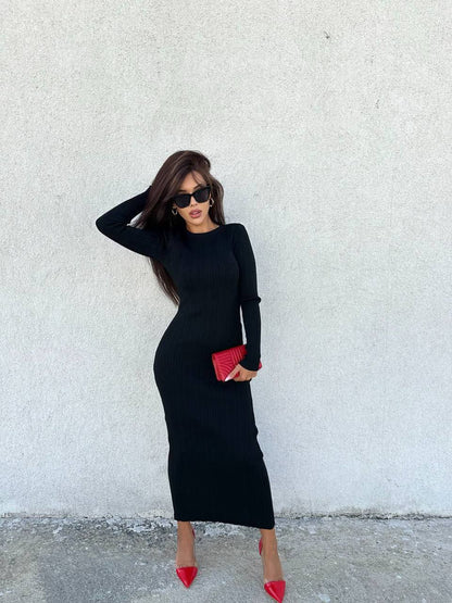 Woman in a black dress with red shoes and clutch against a white wall