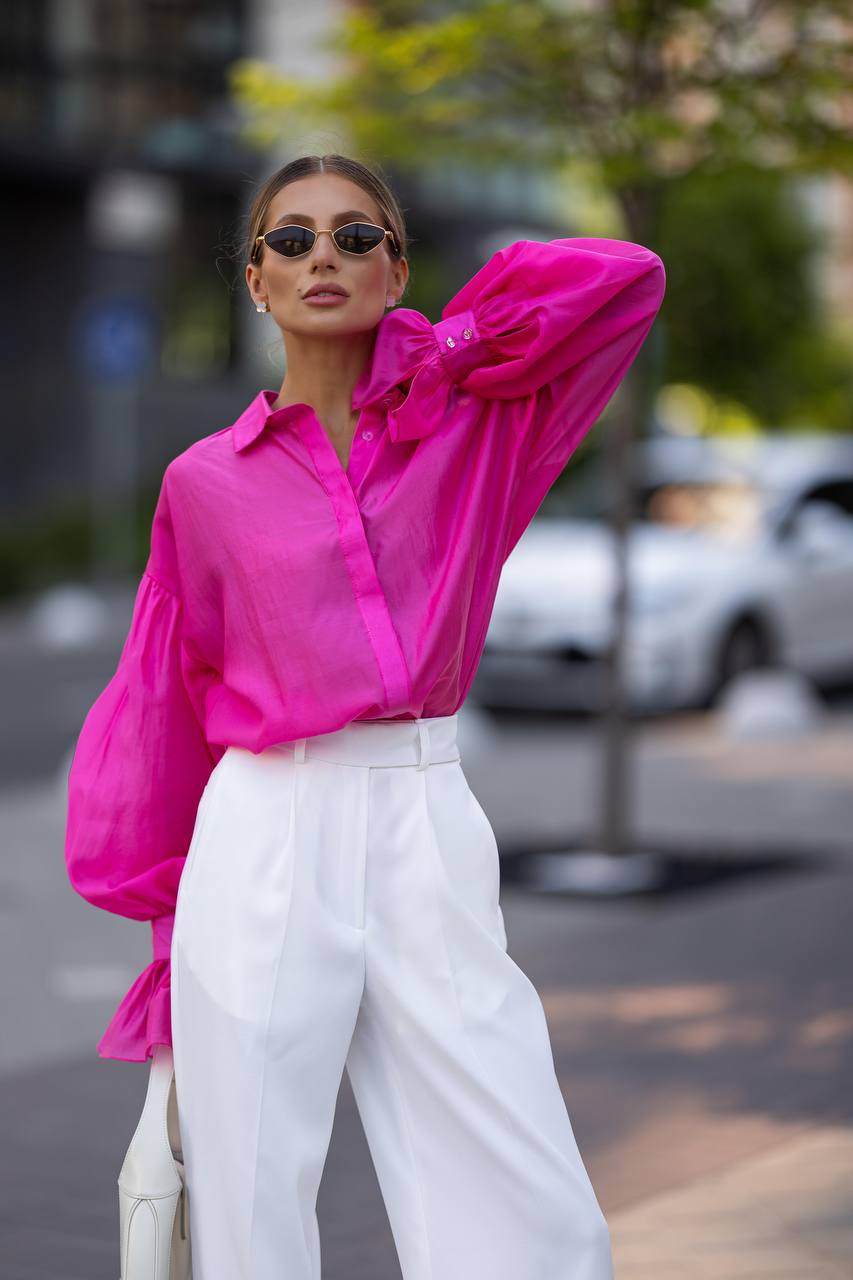Woman wearing a bright pink shirt and white pants on a street.