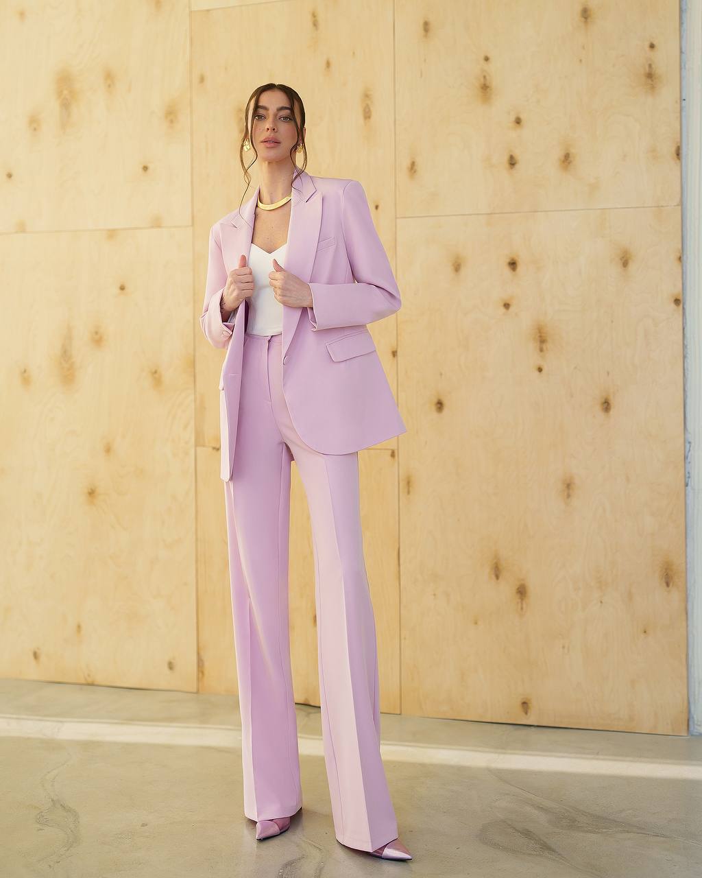 Woman wearing a pastel pink suit standing against a wooden paneled wall.