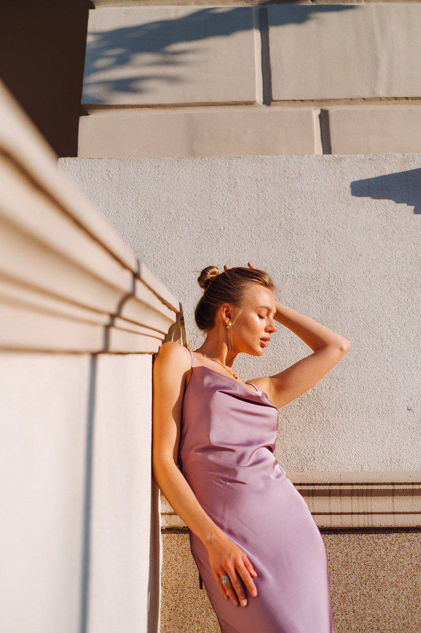 Woman in a purple dress standing against a stone wall.