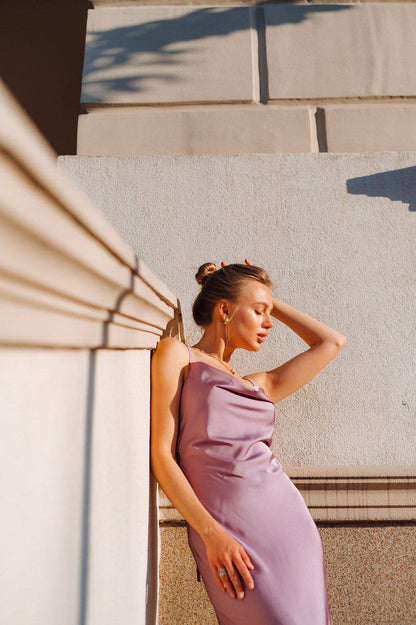 Woman in a purple dress standing against a stone wall.