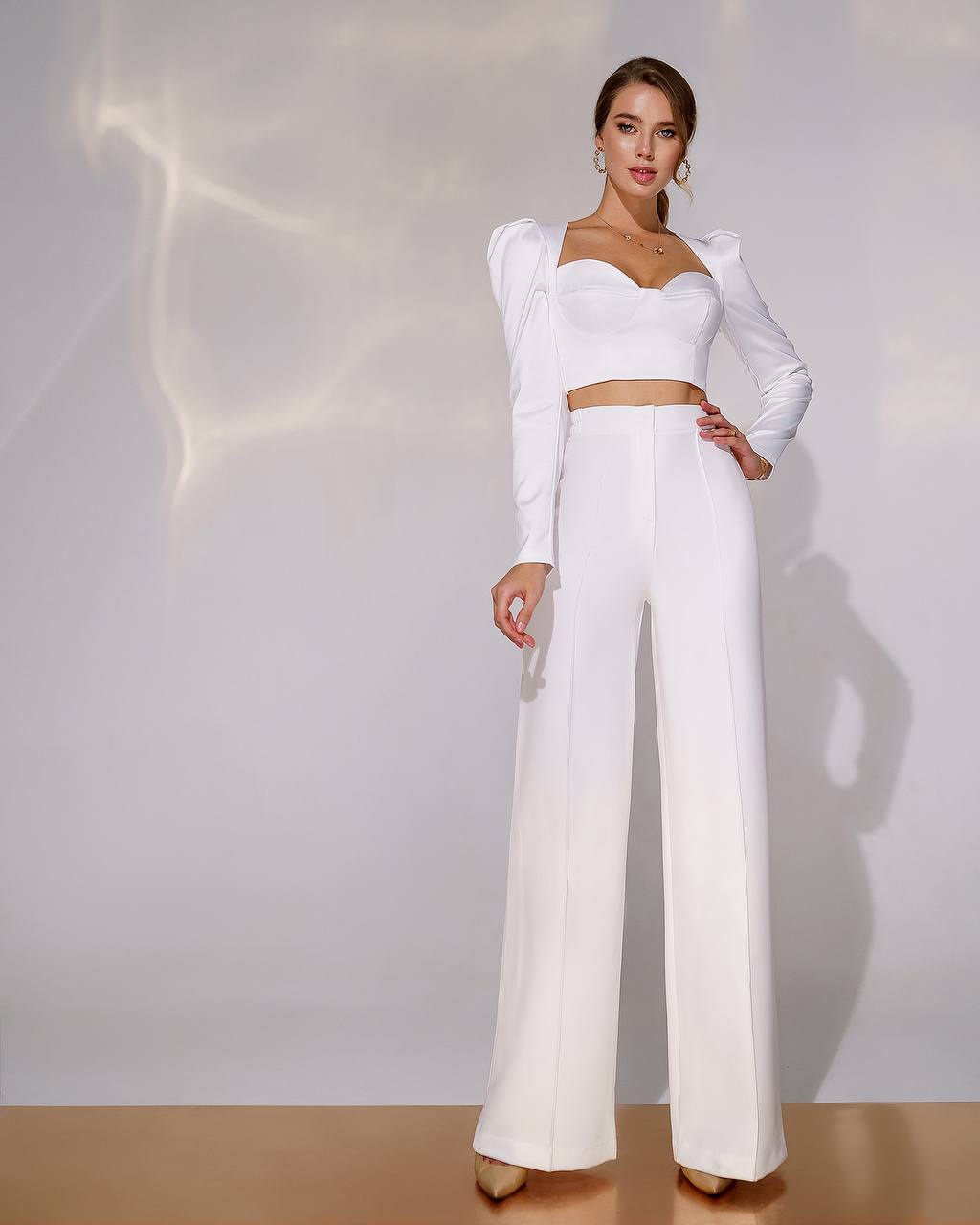 Woman wearing a white outfit with a top and wide-leg pants against a neutral background