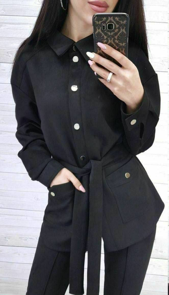 Person wearing a black outfit with white buttons against a light background