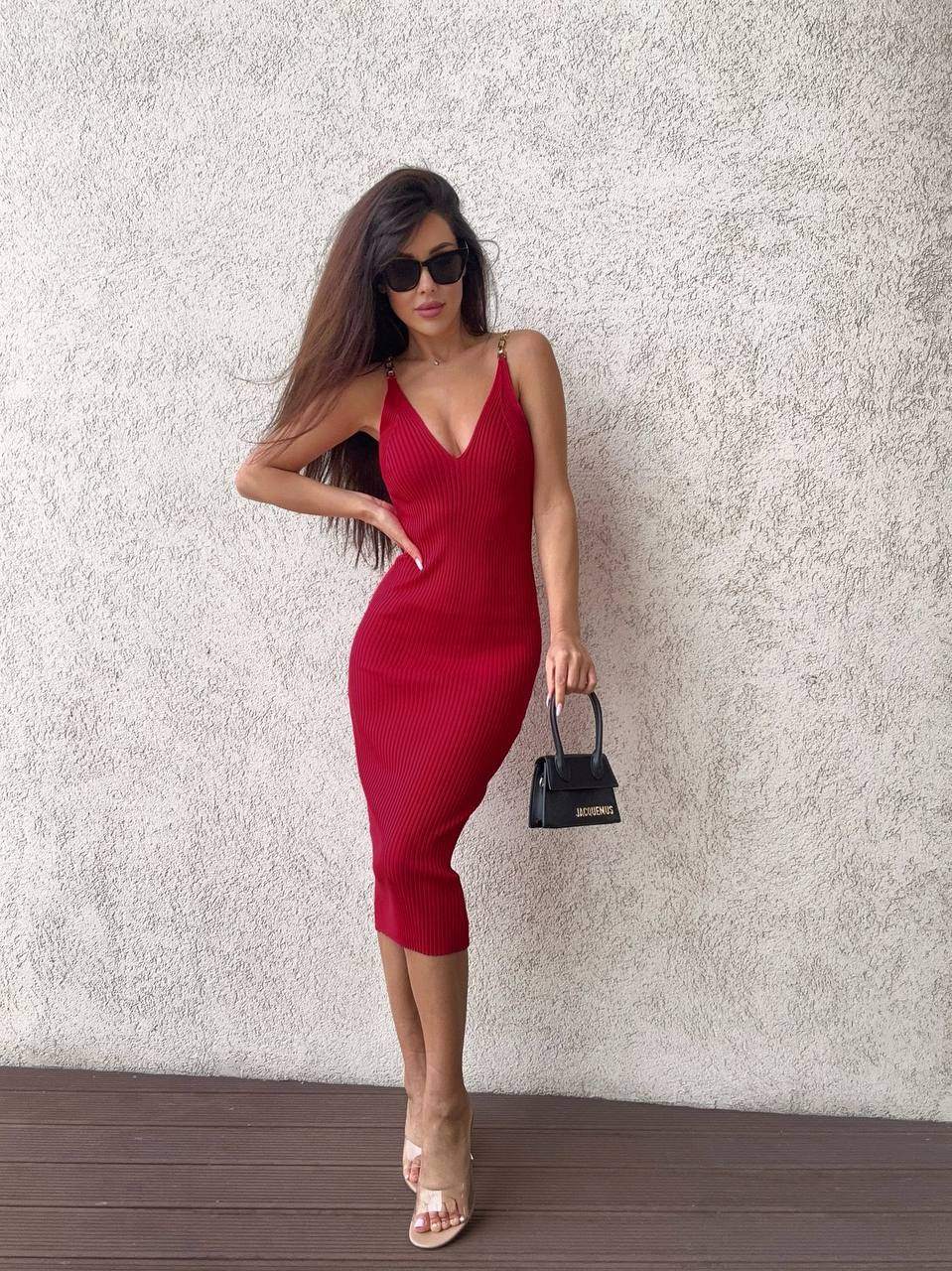 Woman in a red dress holding a black handbag against a textured wall.