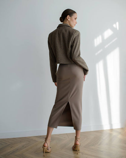 Woman wearing a patterned blazer and brown skirt in a minimalistic room.