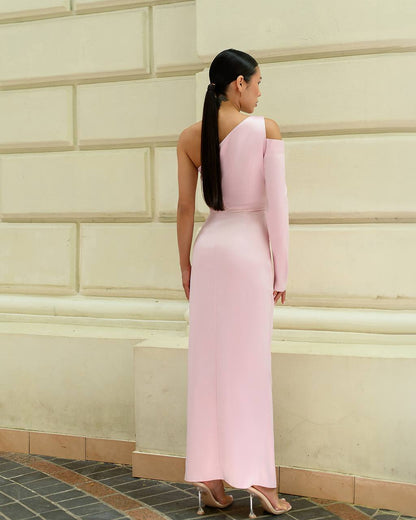 Woman in a pink off-shoulder dress standing against a beige wall.