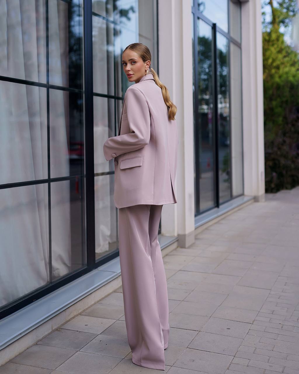 Woman in a pink suit standing outside a building with large windows.