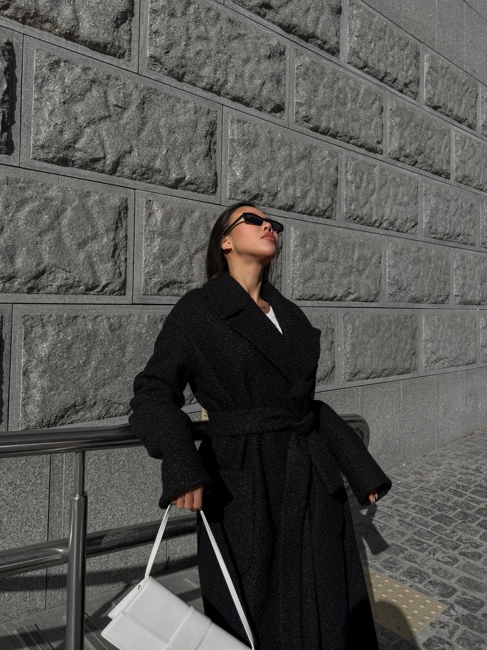 Person wearing a black coat against a textured wall