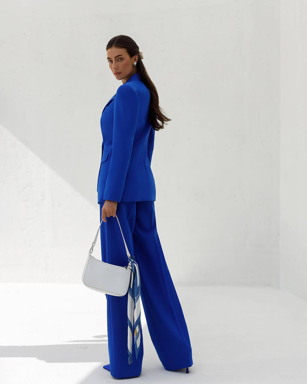 Woman in a blue suit holding a white handbag against a white background