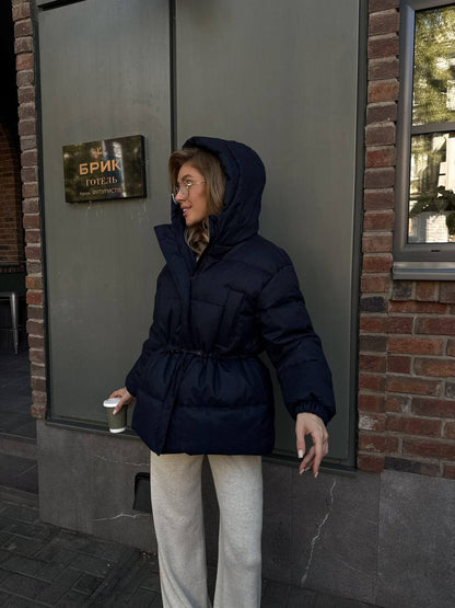 Person wearing a dark blue hooded jacket standing outside a building with a sign.