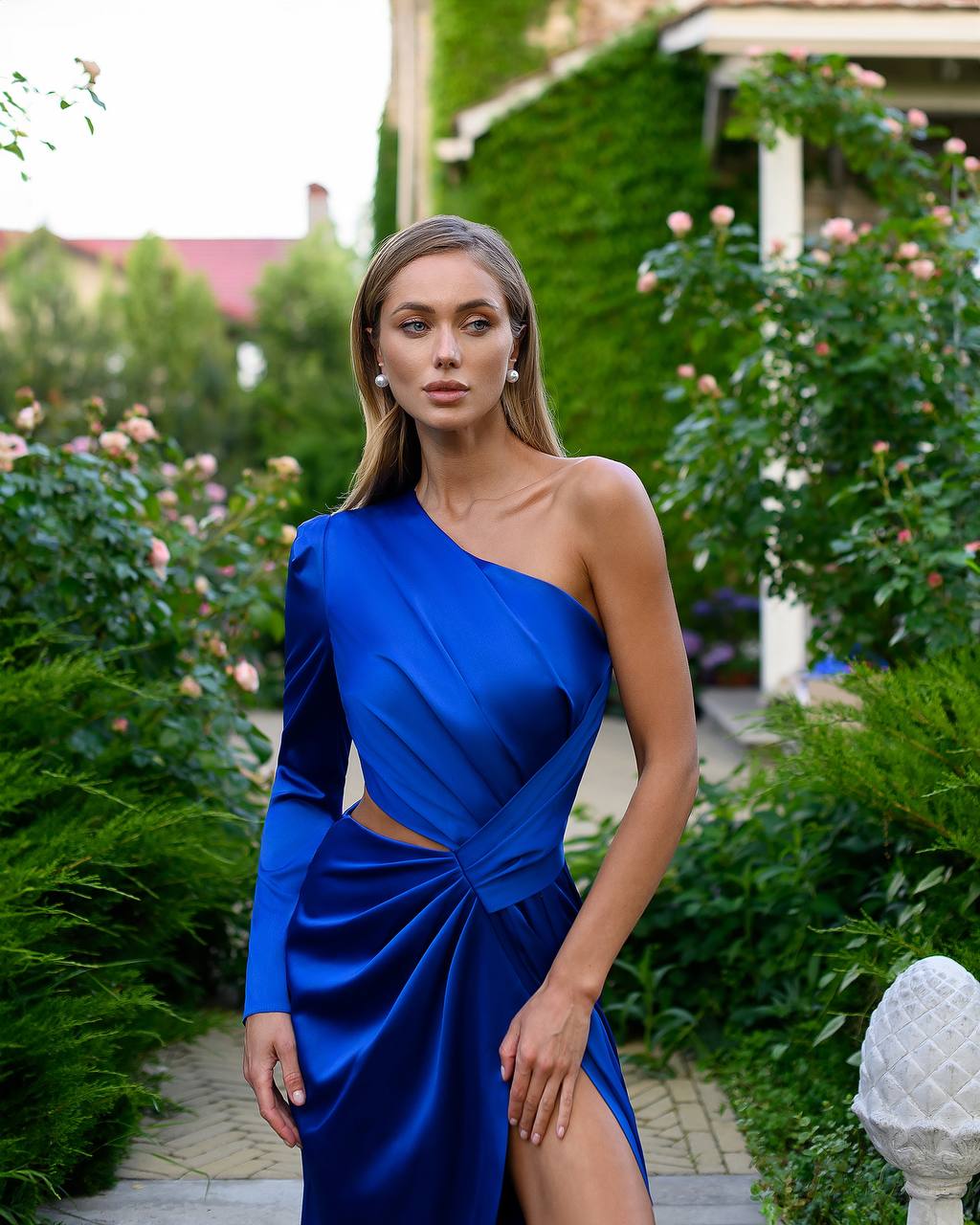 Woman wearing a blue one-shoulder dress in a garden setting