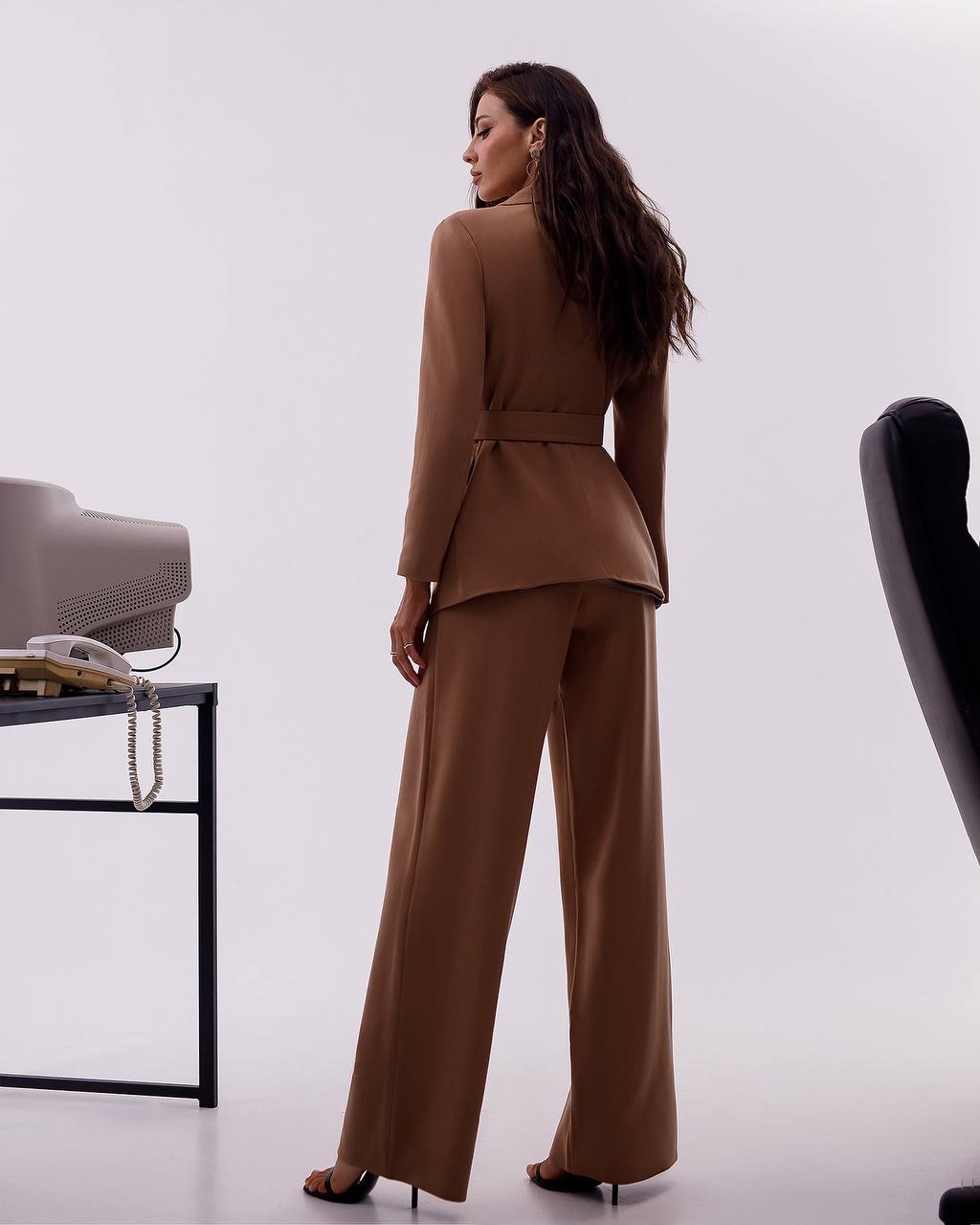 Woman in a brown suit standing in an office setting with a white background