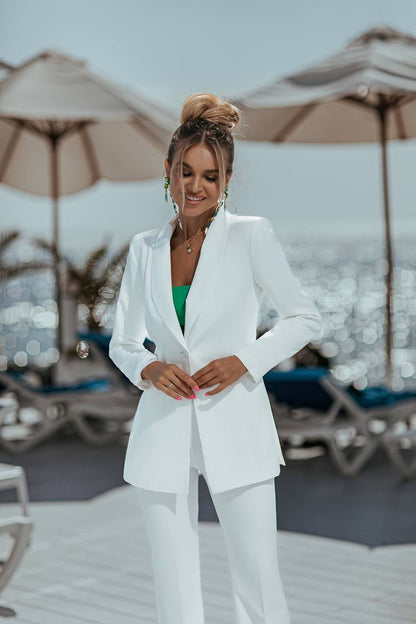 Woman in a white suit standing on a beach with umbrellas and chairs in the background