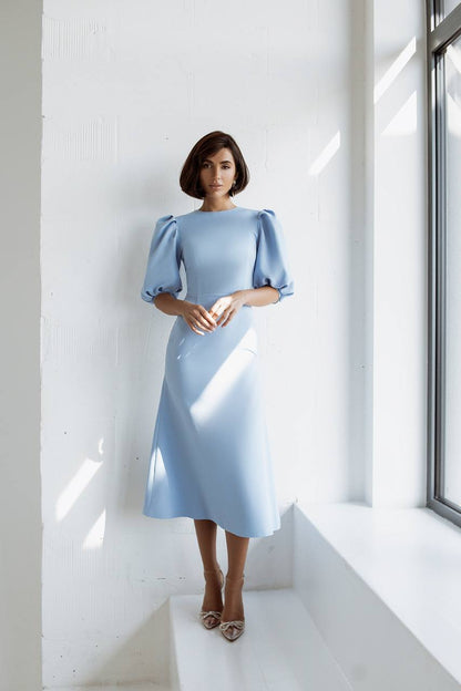 Woman wearing a light blue dress with puffed sleeves in a bright room.
