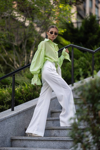 Person wearing a light green blouse and white pants on outdoor steps with greenery in the background