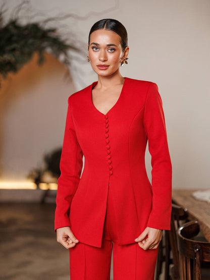 Woman wearing a red suit standing indoors with a blurred background