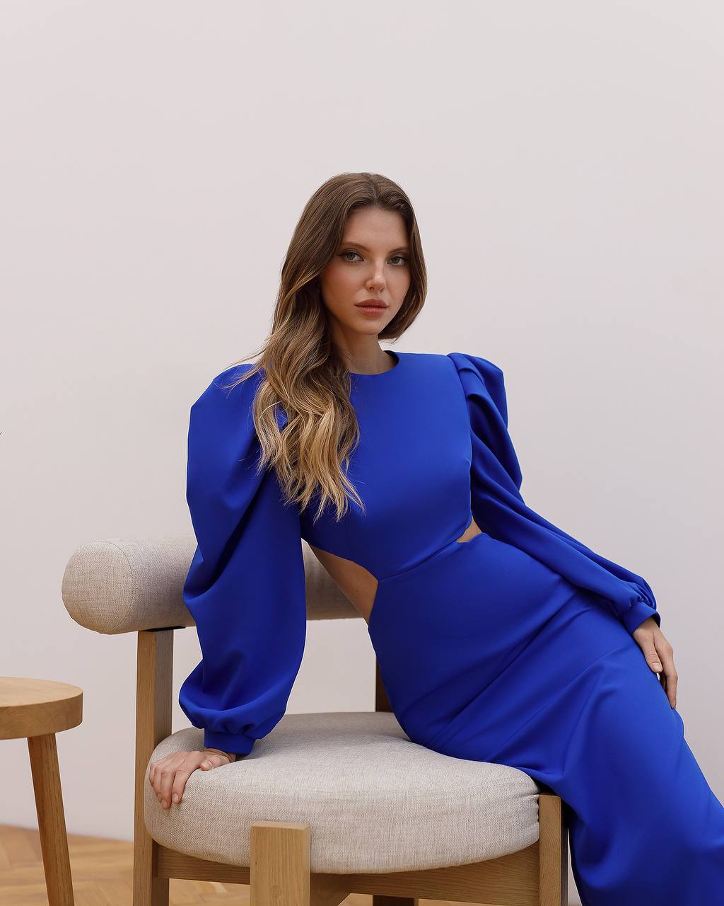 Woman in a blue dress sitting on a chair against a plain background