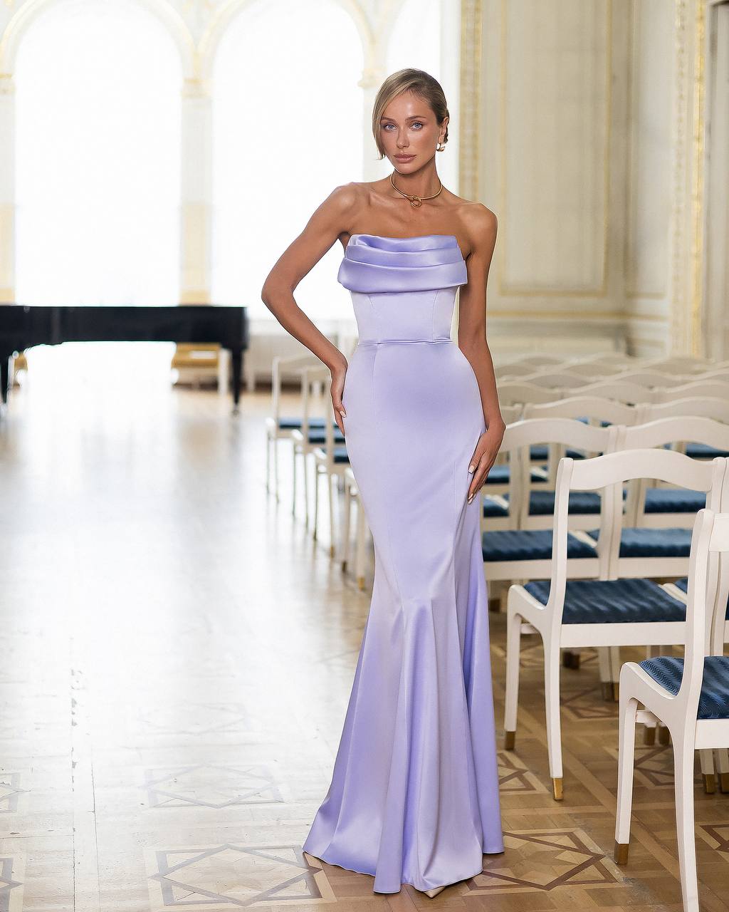 Woman in a strapless lavender gown standing in an elegant room with white chairs and a table.