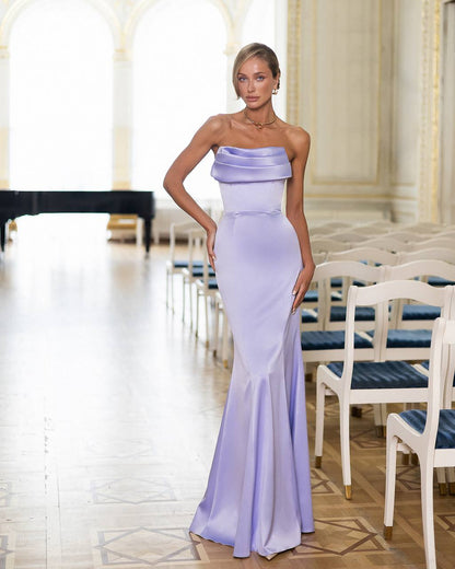 Woman in a strapless lavender gown standing in an elegant room with white chairs and a table.