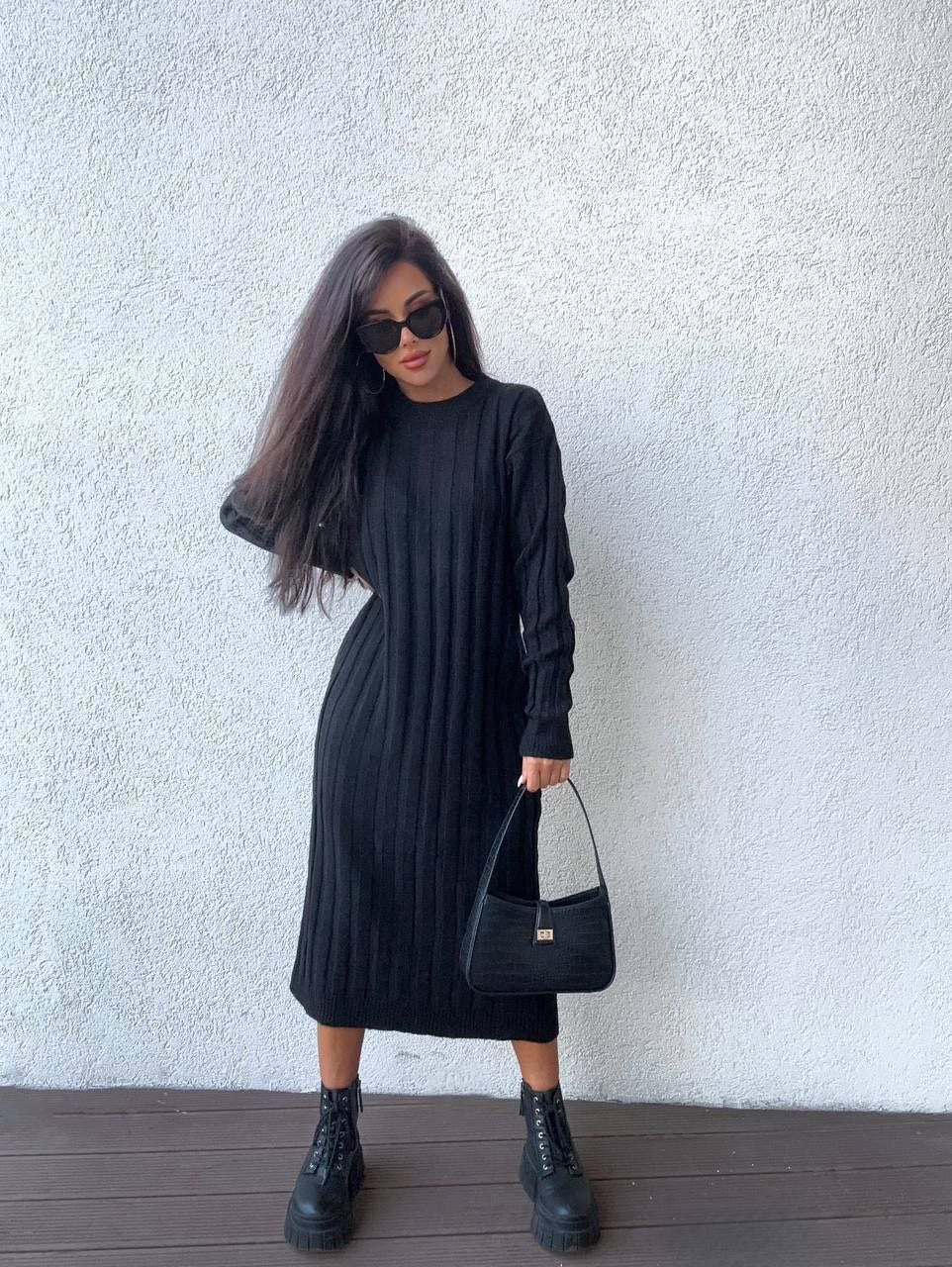 Woman wearing a black dress and boots against a white wall