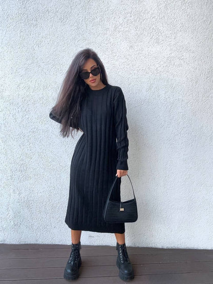 Woman wearing a black dress and boots against a white wall