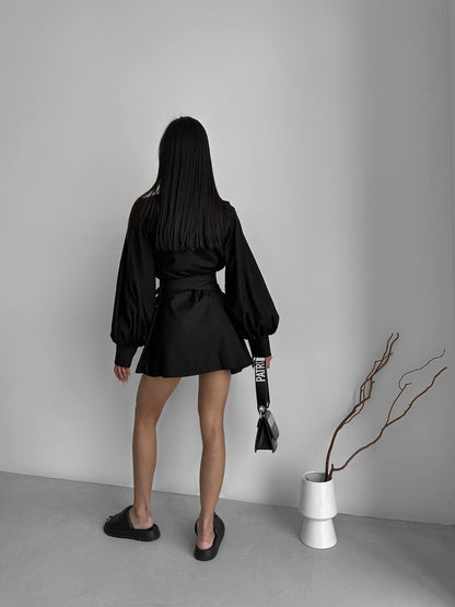 Person wearing a black outfit standing in a minimalistic room with a vase and branch.
