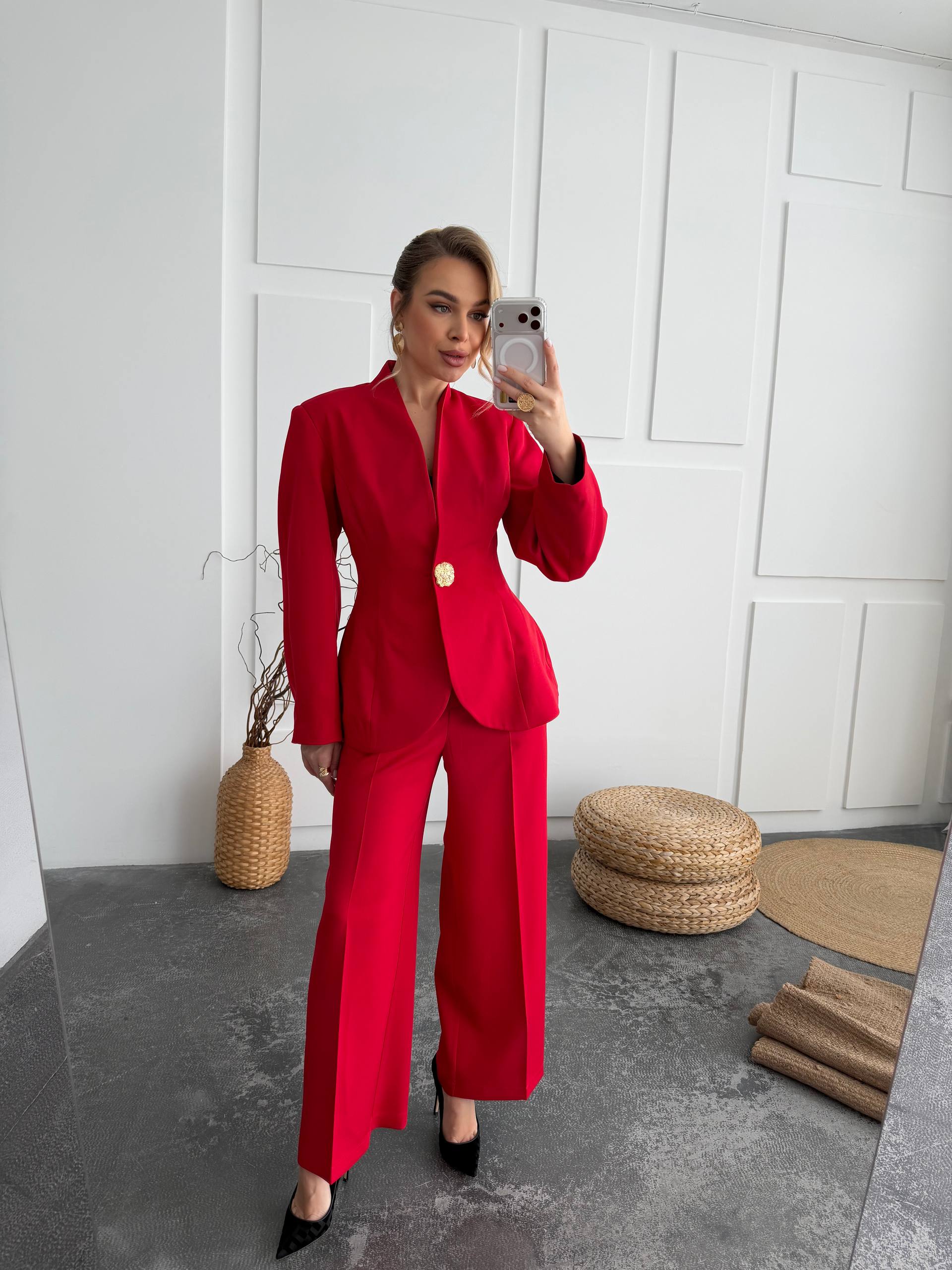 Woman in a red suit taking a mirror selfie in a minimalistic room.