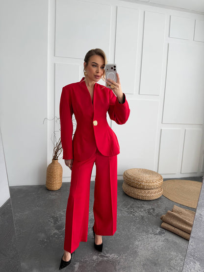 Woman in a red suit taking a mirror selfie in a minimalistic room.