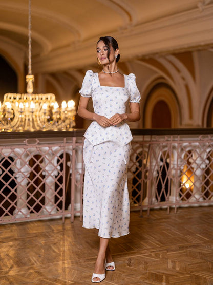Woman in a white dress standing in an elegant indoor setting with chandelier and wooden floor.