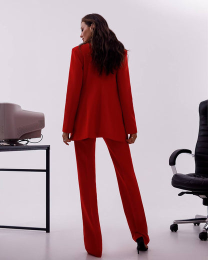 Person wearing a red suit standing in an office setting with a chair and desk.