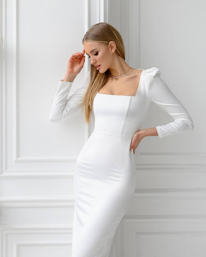 Woman wearing a white dress with long sleeves against a white wall
