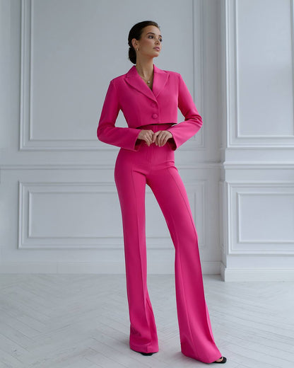 Woman wearing a bright pink suit standing against a white paneled wall.