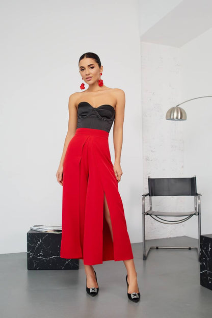 Woman wearing a black strapless top and red wide-leg pants in a minimalistic room.