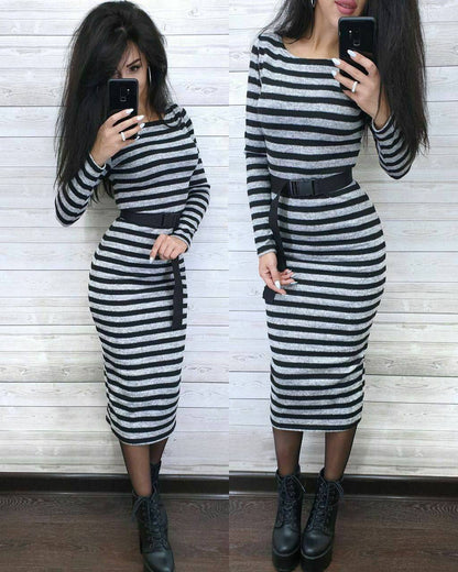 Person wearing a black and white striped dress with a belt, standing against a white wooden panel wall.