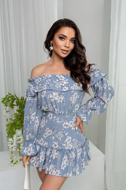 Woman wearing a blue floral off-shoulder dress against a white curtain background
