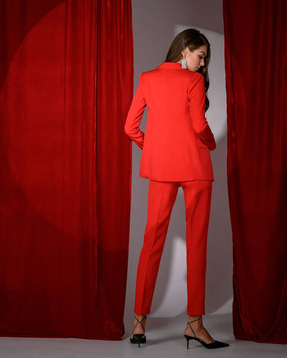 Woman wearing a red suit standing between two red curtains.