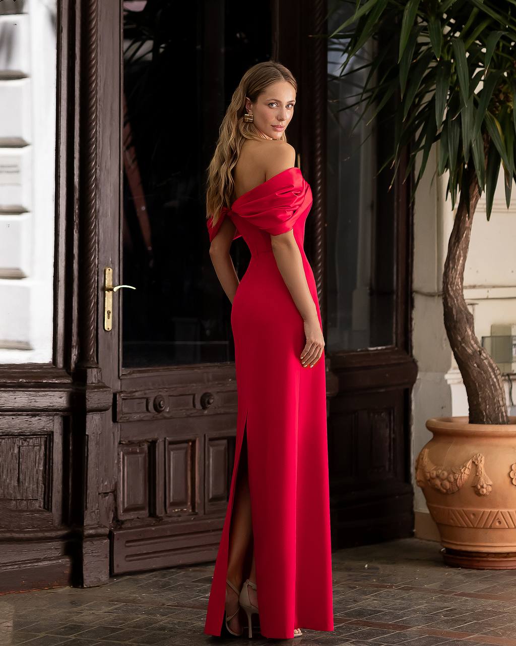 Woman in a red evening gown standing in front of a wooden door.